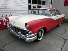 an old red and white car parked in front of a garage