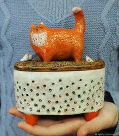 a person holding a ceramic cat on top of a pot with holes in the bottom