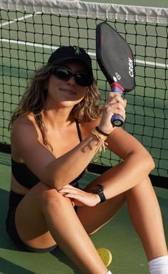 a woman sitting on the ground with a tennis racket in her hand and wearing sunglasses