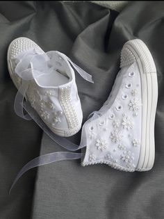 two white shoes with bows and pearls on them sitting on a gray cloth covered bed