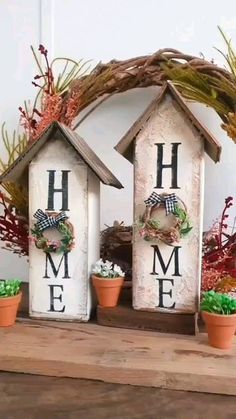 two birdhouses with wreaths on them sitting next to each other in front of some potted plants