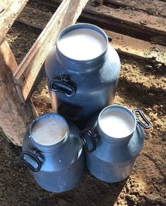 three large metal jugs sitting next to each other on the ground in front of a wooden fence