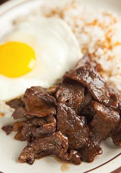 a plate with rice, meat and an egg on it next to a fried egg