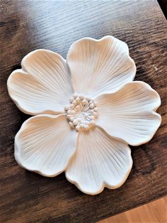 a white flower shaped dish sitting on top of a wooden table next to a knife