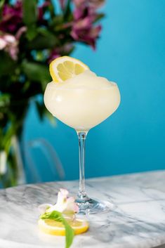 a glass filled with lemonade sitting on top of a marble table next to flowers