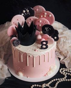 a pink cake with black and white decorations on top, surrounded by pearl necklaces