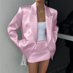 a woman wearing a pink suit and white top standing in front of a wall with her hands on her hips