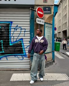 a man standing on the sidewalk in front of a building with graffiti all over it