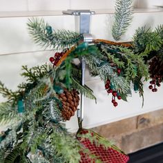 a christmas wreath with pine cones and red berries hanging from the front of a fireplace