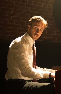 a man in a white shirt and red tie sitting at a piano with his hands on the keyboard