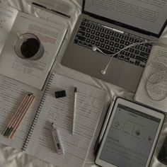 an open laptop computer sitting on top of a bed next to notebooks and pens