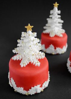 three red cakes decorated with white frosting and gold stars on top, one has a christmas tree in the middle