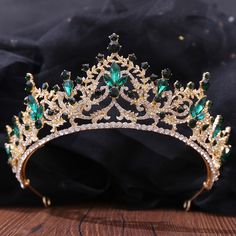 a tiara with green and white stones on it sitting on a wooden table next to a black cloth