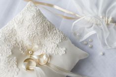 a white wedding ring pillow on top of a bed next to a satin ribbon and pearls