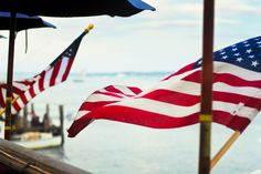 an american flag is flying in the wind near some umbrellas and boats on the water