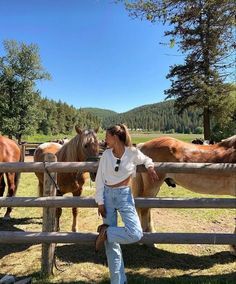 a woman standing in front of horses behind a fence