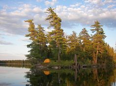 an island in the middle of a lake with trees around it and a tent on top