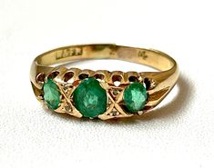 Victorian circa 1870s emerald and diamond trilogy ring in 18ct yellow gold The claw-set gemstones are earth-mined The three oval deep green emeralds (AA natural, not doublets) are well-cut and have good transparency, the central stone is 0.4 carat and the two sides stones are 0.2 carat each, total weight .80 ctw There are four rose-cut accent diamonds Stamped "W&FR" which stands for Walter & Frank Rabone, Birmingham-based gold- and silversmiths active from the early Victorian era The gold grade Victorian Oval Yellow Gold Emerald Ring, Victorian Oval Emerald Ring In Yellow Gold, Heirloom Oval Emerald Ring With Three Stones, Oval Three Stone Emerald Ring In Yellow Gold, Diamond Trilogy Ring, Trilogy Ring, Multi Stone Ring, Multi Stone, 2 Carat