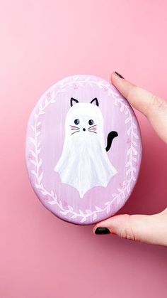 a woman's hand holding up a small button with a white cat on it