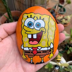 a hand holding an orange painted rock with a cartoon character on it