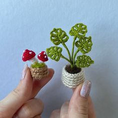 two tiny crocheted plants with leaves and mushrooms in them are being held by someone's hands