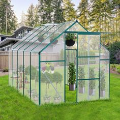 a green house with plants in it on the grass near a fence and houses behind it