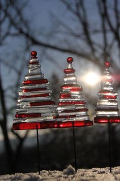 three red and silver christmas trees on top of snow covered ground with sun shining behind them