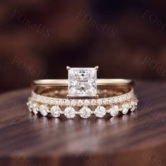 two wedding bands with a princess cut diamond in the center on top of a wooden table