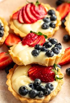 small tarts with fruit on them sitting on a table next to strawberries and blueberries