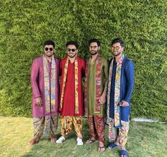 three men standing next to each other in front of a green wall wearing colorful clothing