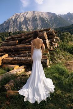 a woman in a wedding dress is looking at the mountains and logs that are stacked on top of each other