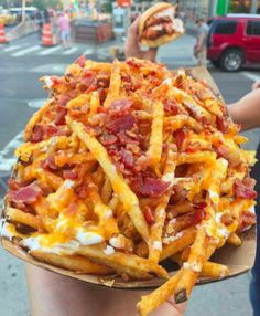 a person holding up a plate full of french fries covered in cheese and bacon