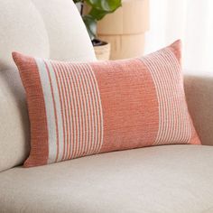 an orange and white striped pillow sitting on top of a couch next to a potted plant