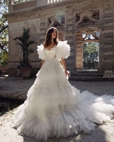 a woman in a white wedding dress standing on a stone walkway with an old building in the background