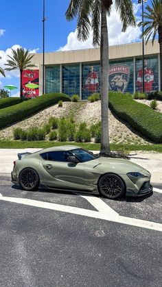 a green sports car is parked in front of a building with palm trees and bushes