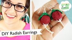 a woman wearing glasses and holding up two red strawberry earrings with green leaves on them