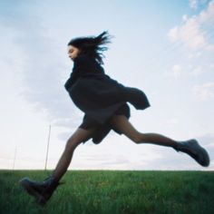 a woman is running through the grass with her hair in the air and she's wearing boots