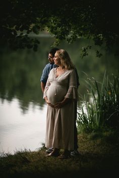 a pregnant woman standing next to a man in front of a body of water at night