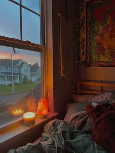 two lit candles sit on a window sill in front of a bed with blankets