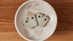 three leather tags in a white bowl on a wooden surface