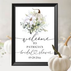 a welcome sign with white pumpkins and greenery on the front, in black frame