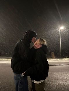 a man and woman standing in the rain at night with their arms around each other