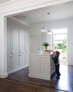 a young boy standing in front of a white kitchen island with drawers and cupboards