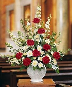 a white vase filled with red and white flowers on top of a wooden table next to pews