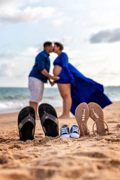 a couple kissing on the beach with flip flops and sandals in front of them