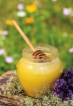 a jar filled with honey sitting on top of a wooden table next to purple flowers