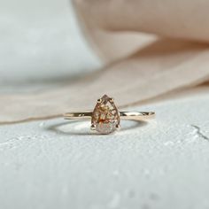 an engagement ring with a pear shaped diamond in the center on a beige cloth background