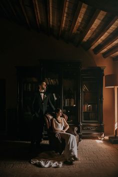 a bride and groom sitting on a chair in front of a bookcase at night