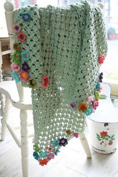 a green crocheted blanket with flowers on it sitting on a chair in front of a window