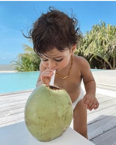 a baby in a bathing suit drinking from a coconut